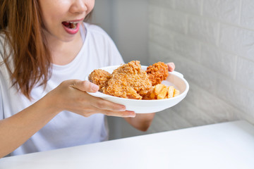 Young Aisan woman in white T-shirt holding a plate of her favourite fried chicken, french fries. Unhealthy food concept. Close up