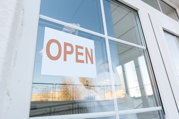 Naklejka premium Business office or store shop is open business of novel Coronavirus COVID-19 pandemic. Unidentified person wearing mask hanging open sign in background on front door.