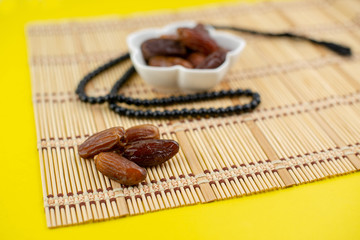 Ramadan Kareem Festival. Close up of dried dates fruit in bowl with rosary on yellow background. Selective focus.