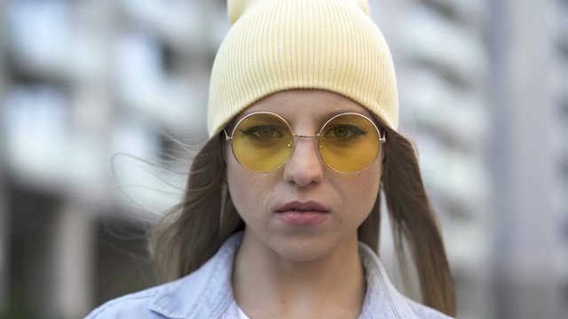 4k. Pretty young girl in yellow cap and glasses stand in city area. Street portrait