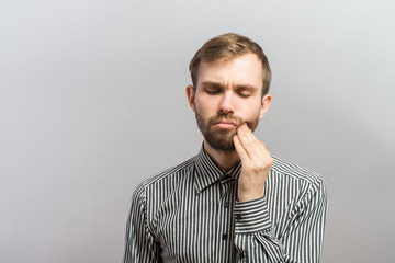a young man with a beard in shirt feels toothache