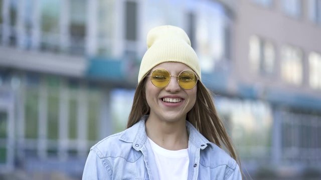 4k. Real young girl  in yellow cap and glasses laughs in city area. Street portrait

