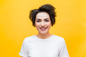 Young happy brunette woman with a short haircut in a white T-shirt on a yellow background. portrait...
