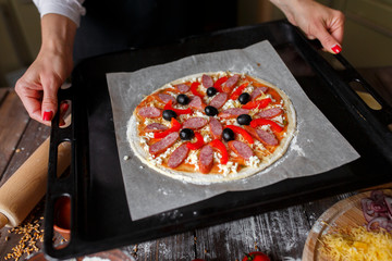 Raw pizza with ingredients and tomato, spices, sausages on baking tray
