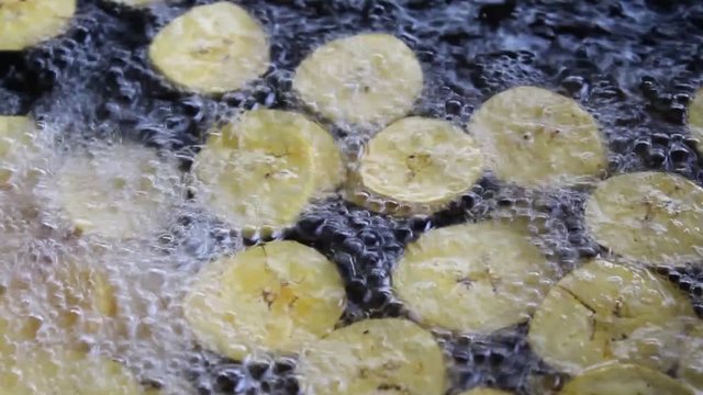 cooking fried plantains, fried plantains floating in boiling oil, close shot to fried plantains, banana chips in boiling oil. cooking chifles.