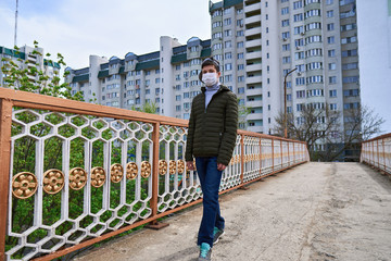 teen boy walks down the street during the day, a pedestrian walkway and high-rise buildings with apartments, a residential area, a medical mask on his face protects against viruses and dust