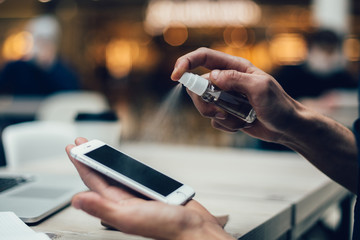 close up . cafe visitor spraying antiseptic on his smartphone