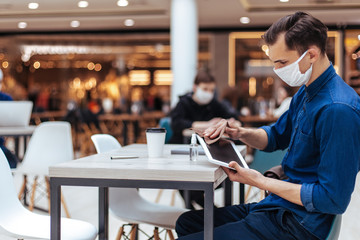 man in protective mask wiping the screen of a digital tablet with antiseptic