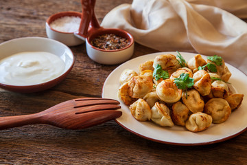Dumplings with meat, onion and sour cream, on a plate, on wooden background