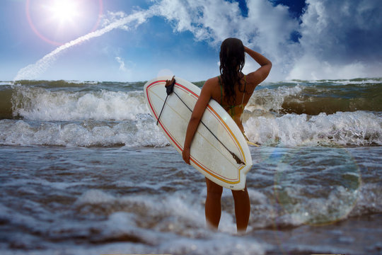 Frau mit Surfbrett schaut auf das offene Meer