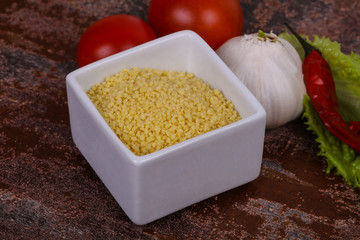 Raw couscous in the bowl served salad leaves, tomato and pepper