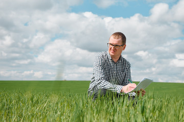 Young farmer on a wheat field. Young wheat in spring. Agriculture concept. An agronomist examines the process of ripening wheat in the field. The concept of the agricultural business.