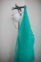 A disposable scrub and a face-mask hanging on a hook.
