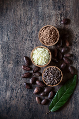 Cacao products  - powder, butter, whole beens, nibs, original leaves on old rustic background.