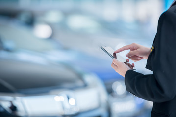 Women car salesmen use mobile smartphones at car showrooms. Check car sales in mobile phones to sell new cars.
