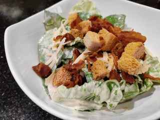 Caesar salad with lettuce, croutons, crispy bacon and parmesan cheese. serving on white ceramic bowl