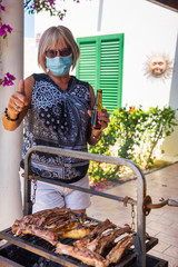 elderly lady cooking on a barbecue with face mask