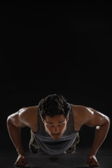 Fototapeta na wymiar Man doing push ups in front of a dark background. 
