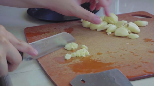 Footage of lady hand peeling garlic using knife.