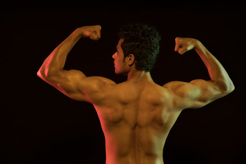 Bare chested man flexing his muscles in front of a dark background. 
