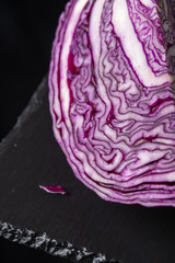 Obraz premium Close-up of open red cabbage, on black slate and black background, vertically