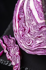 Obraz premium Top view of open red cabbage, with pieces, and selective focus, on black slate and black background, vertical