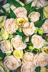 Close-up of a cream rose wedding bouquet with wedding rings lying on top of it.