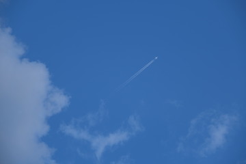 a plane is flying very high on the blue sky, leaving a trail behind it
