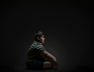 Young boy sitting on the floor while being lost in his thoughts. (Obesity)

