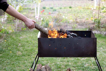 Unrecognizable man putting firewood into a barbecue stove in his garden. Spring outdoor recreation. Picnic in the country. kindling the fire.Barbeque in nature. Picnic preparation. Firewood 