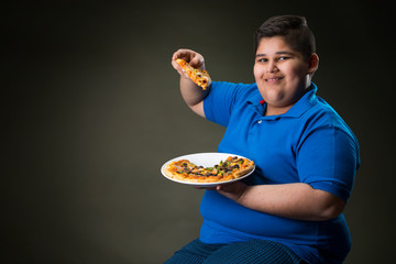 Young boy sitting with a plate full of pizza. (Obesity) 	