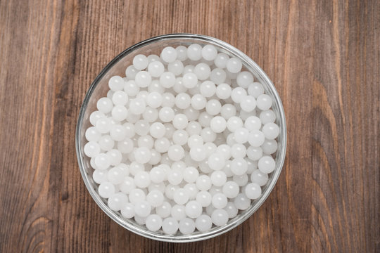 hydrogel white balls in glassware on wooden board. artificial moisture-absorbing material that contributes to accumulation and preservation of moisture. used for planting plants or children games