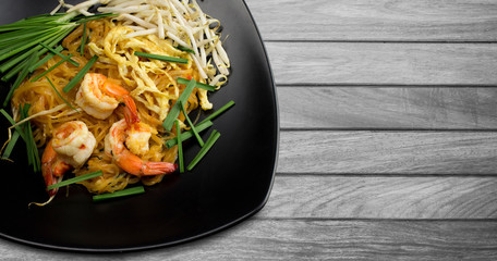 Stir fried noodles with prawns (Pud Thai) in black dish on wooden table