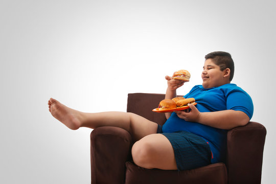 Young boy sitting on the sofa at home with a plate full of burgers. (Obesity) 	