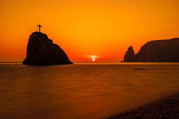 View of the sunset sea and the beach, the volcanic rock is lit by the warm sunset, sand and...