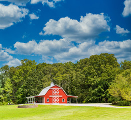 Fototapeta na wymiar An old red, wooden barn on a green, grassy hill under nice skies