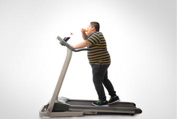 Fototapeta na wymiar Young boy walking on the treadmill while eating a slice of pizza. (Obesity) 