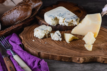 Cheese and bread on a wooden stand on the table dark background. The concept of nutrition and beautiful serving of food.