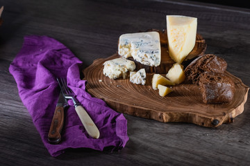 Cheese and bread on a wooden stand on the table dark background. The concept of nutrition and beautiful serving of food.