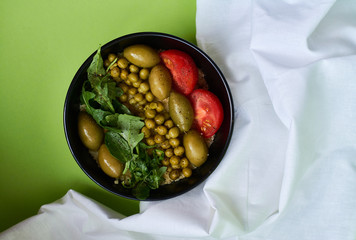Green summer background and white cloth with  black bowl and delicious useful breakfast of porridge and vegetables. Tomatoes, olives, arugula, peas.