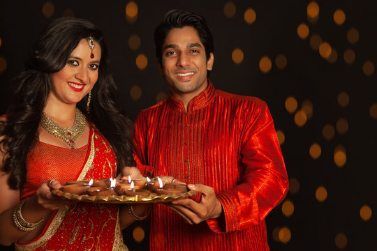 Young couple holding a tray of diyas together on the occasion of Diwali. (Couple)