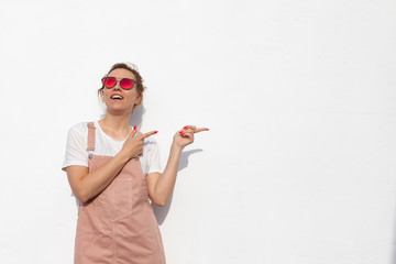 Excited young woman in glasses pointing her index finger sideways, raising eyebrows and keeping mouth wide opened, showing something surprising on white background