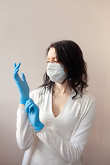 A woman in gloves and a protective mask stands on a light background in a white jacket. The concept of suppression of coronavirus