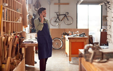 Male Business Owner In Workshop Making Call On Mobile Phone