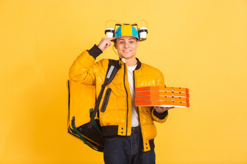 Holding pizza, pointing at head. Emotions of caucasian deliveryman isolated on yellow background. Contacless delivery service during quarantine. Man delivers food during isolation. Safety. Hurrying up