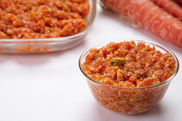 Gajar ka halwa in a glass bowl kept in front of carrots and a serving bowl. 
