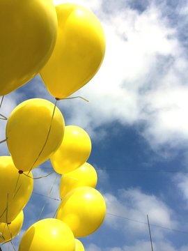 Low Angle View Of Yellow Balloons In Mid-air Against Cloudy Sky