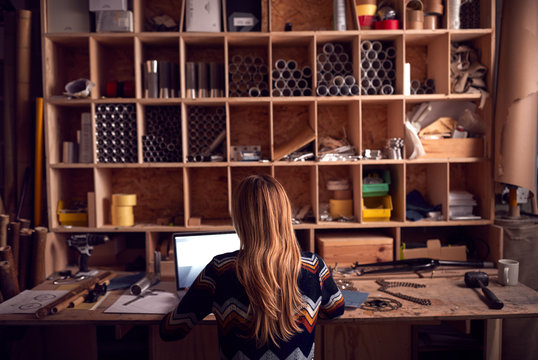 Female Business Owner Working Late In Carpentry Workshop Using Laptop