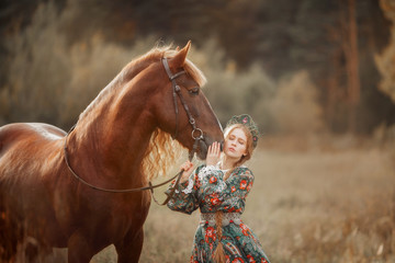 Fototapeta premium Beautiful long-haired blonde young woman in national russian style with red Vladimir draft horse in autumn forest