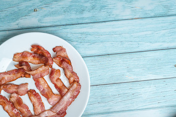 Cooked fired bacon rashers white dish and blue wooden background, Morning Breakfast Concept, View from Top, Flat Lay 